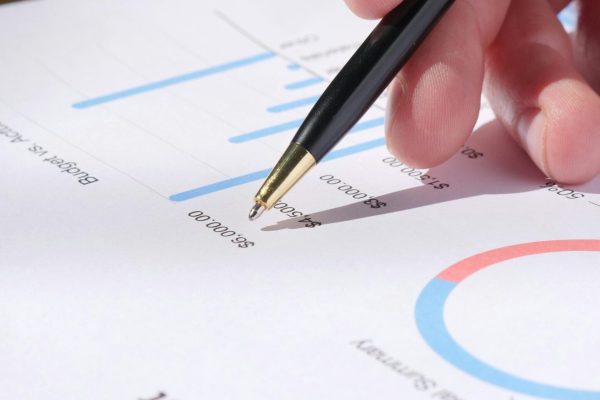 Close-up of hand analyzing data on a monthly budget document with graphs and charts.